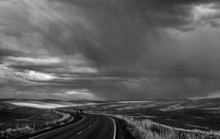 Black and white photo of a road under storm clouds