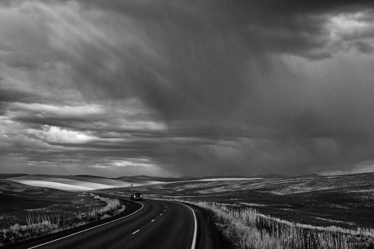 Black and white photo of a road under storm clouds